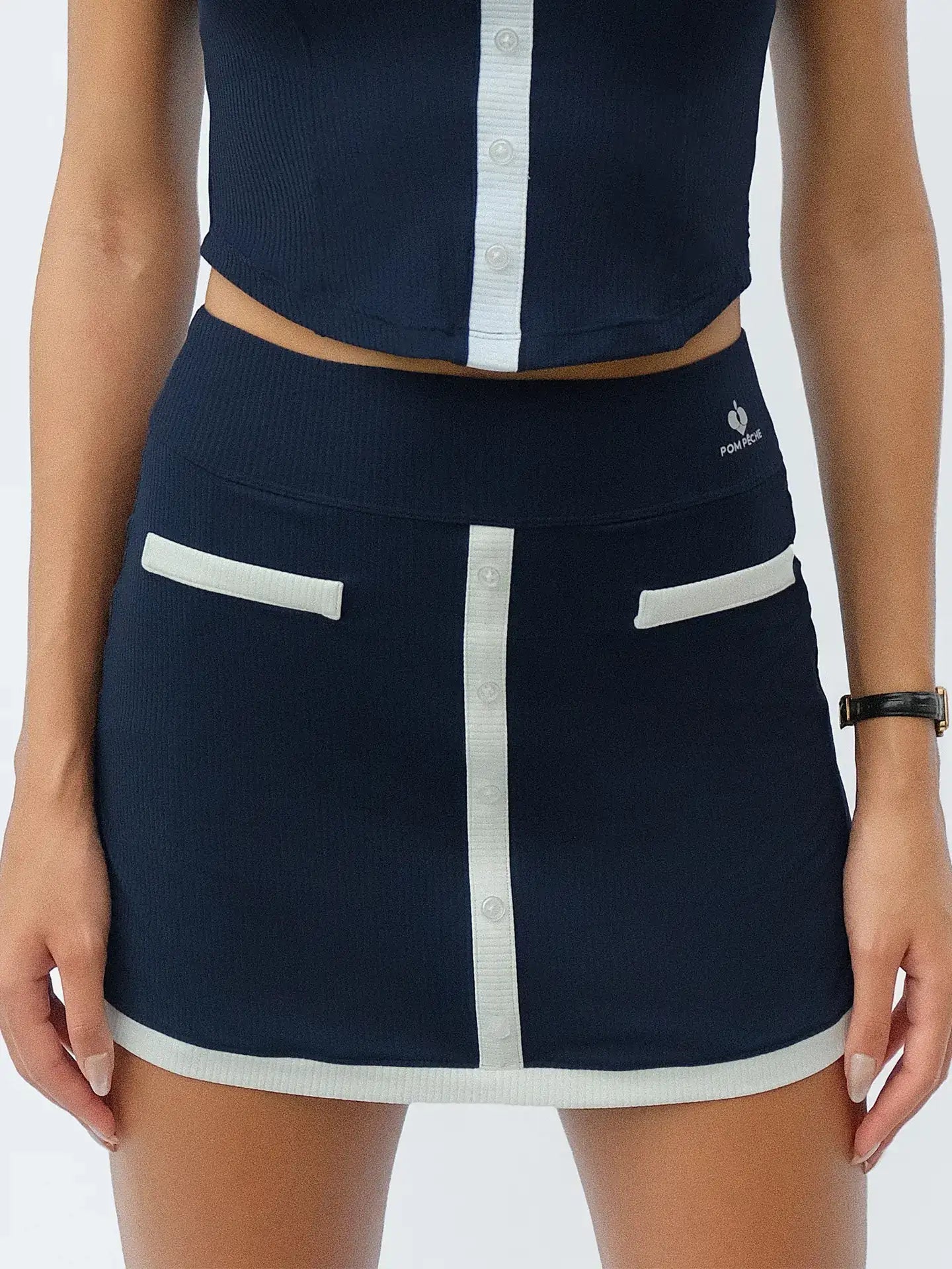 Navy blue tennis mini skirt with contrast trims and button-front detail, offering a neat, preppy look for court or casual wear.