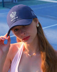 Navy blue tennis baseball cap with embroidered Pom Pêche logo and detachable ribbon.