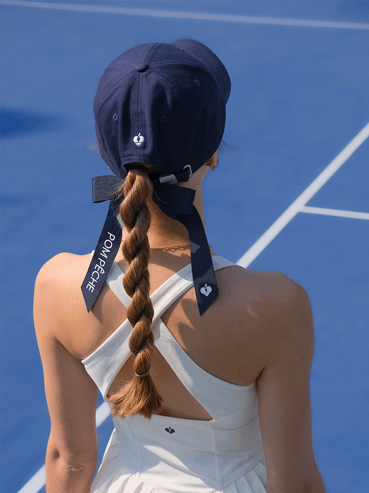 Navy blue tennis baseball cap with embroidered Pom Pêche logo and detachable ribbon.