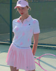 White and pink checkered polo top with diamond pattern and subtle logo, styled on the tennis court.