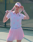 White and pink checkered polo top with diamond pattern and subtle logo, styled on the tennis court.