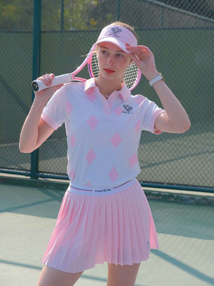 White and pink checkered polo top with diamond pattern and subtle logo, styled on the tennis court.