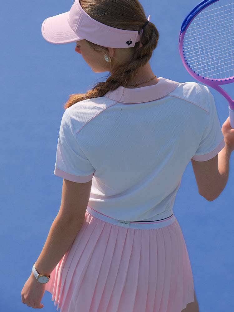 White and pink checkered polo top with diamond pattern and subtle logo, styled on the tennis court.
