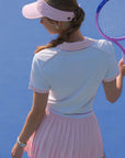 White and pink checkered polo top with diamond pattern and subtle logo, styled on the tennis court.
