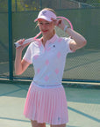 White and pink checkered polo top with diamond pattern and subtle logo, styled on the tennis court.