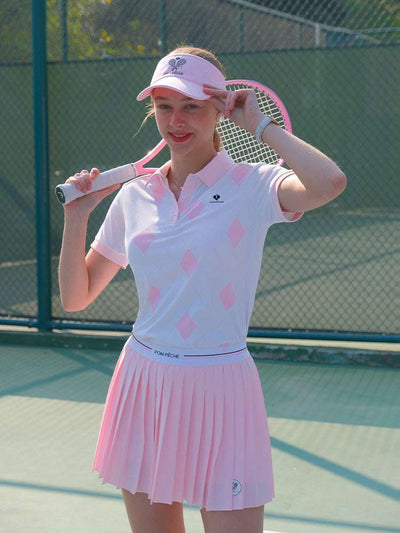 White and pink checkered polo top with diamond pattern and subtle logo, styled on the tennis court.
