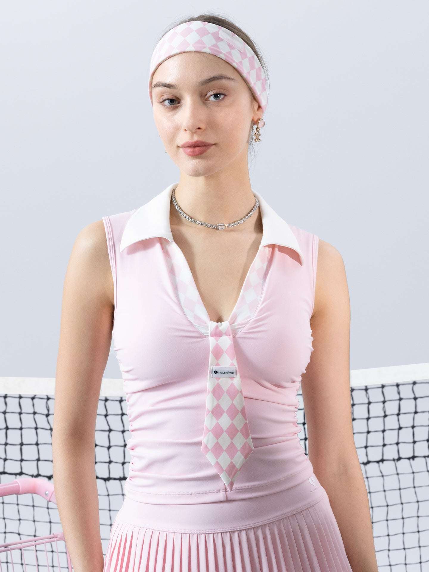 Soft pink slim-fit tennis top with a playful diamond-pattern tie detail, styled for a chic on-court look.