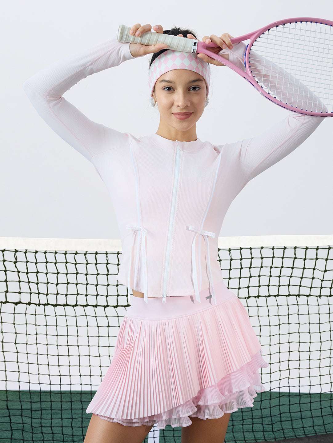 Pink sun-protective tennis jacket with a sculpted fit, adjustable waist ties, and dual ball pockets.