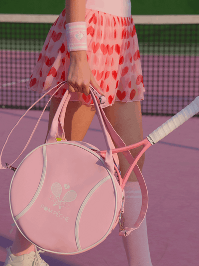 Pink round tennis bag with handles, featuring brand logo and racket-shaped zipper.