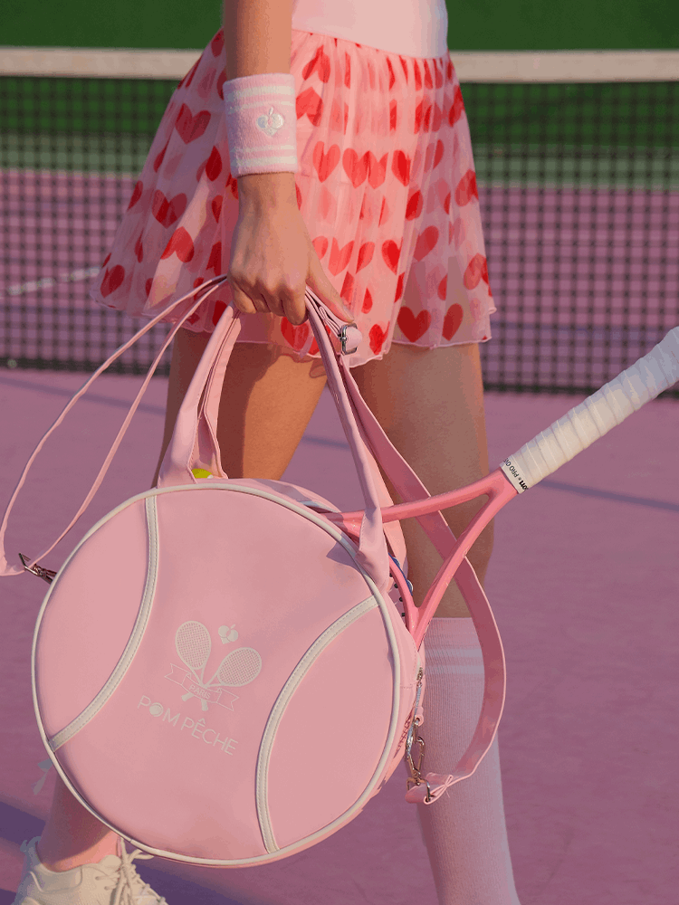 Pink round tennis bag with handles, featuring brand logo and racket-shaped zipper.
