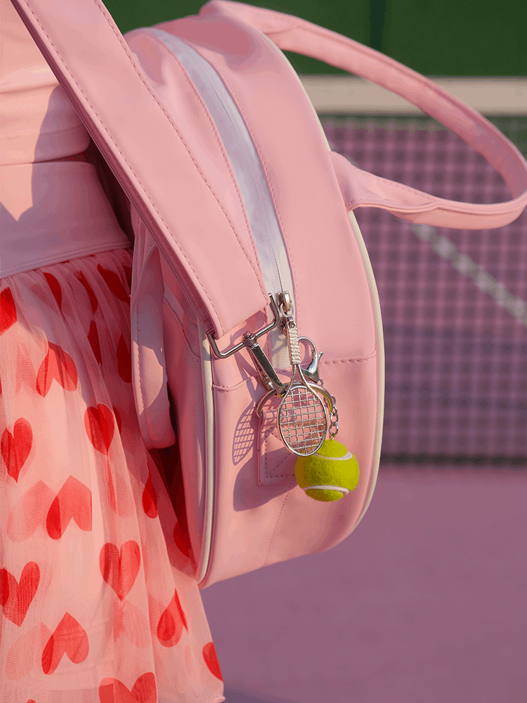 Pink round tennis bag with handles, featuring brand logo and racket-shaped zipper.