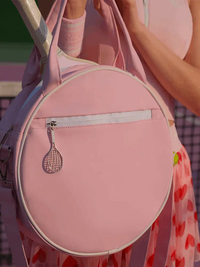Pink tennis bag with a racket charm held by a person wearing a pink outfit.