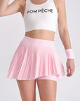 White pleated tennis skirt with red and blue stripes, styled with crop top and visor on a scenic bridge backdrop