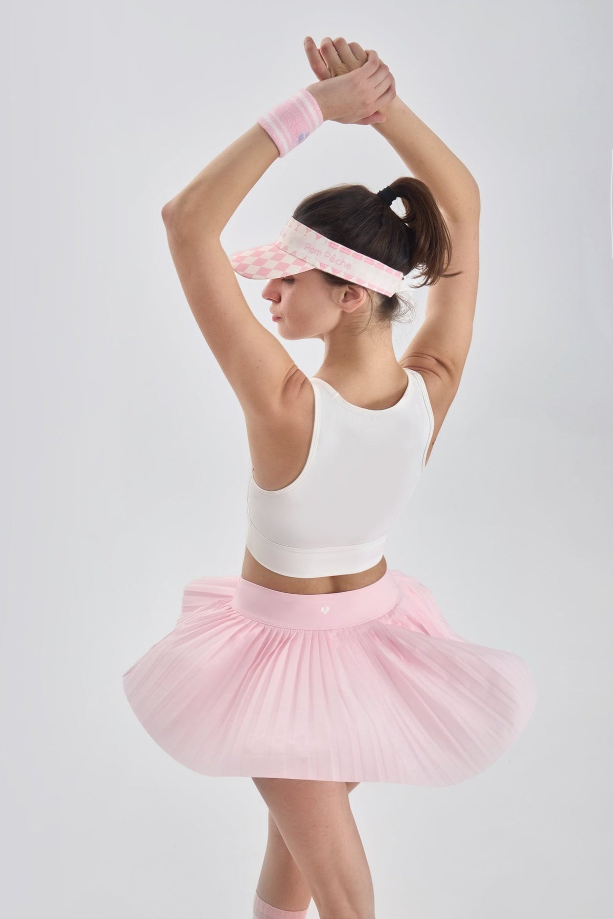 Back view of pink pleated skirt in motion, flaring gently as model raises arms to show flow and flexibility