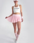 Full body shot of model lifting skirt hem playfully, revealing crisp pleats and matching sporty accessories
