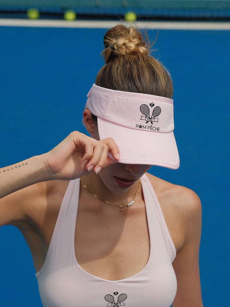 Pink tennis visor with embroidered Pom Pêche logo, white trim, and detachable ribbon at the back.