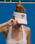 Pink tennis visor with embroidered Pom Pêche logo, white trim, and detachable ribbon at the back.
