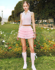 Soft pink cropped tennis top with ruffled collar and sleeveless design, featuring a subtle logo for a chic, sporty look.