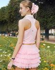 Soft pink cropped tennis top with ruffled collar and sleeveless design, featuring a subtle logo for a chic, sporty look.