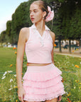 Soft pink cropped tennis top with ruffled collar and sleeveless design, featuring a subtle logo for a chic, sporty look.
