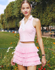 Soft pink cropped tennis top with ruffled collar and sleeveless design, featuring a subtle logo for a chic, sporty look.