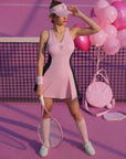 Pink V-neck tennis dress with black curved side panels, styled on the court.