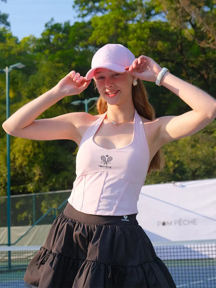 Woman adjusting a pink cap on a tennis court with trees in the background