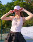 Woman adjusting a pink cap on a tennis court with trees in the background
