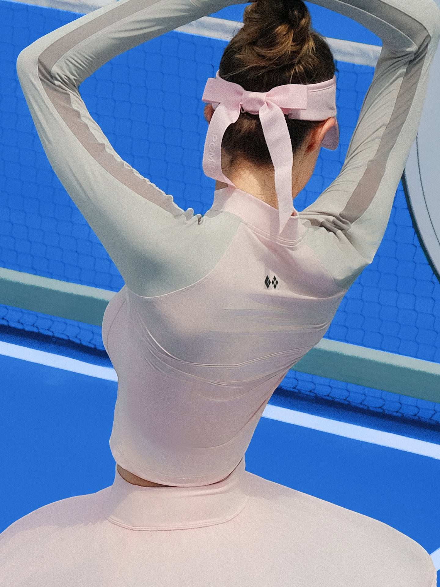 Pink long-sleeve fitted top with a half-zip neckline and subtle logo detail, styled on the tennis court.
