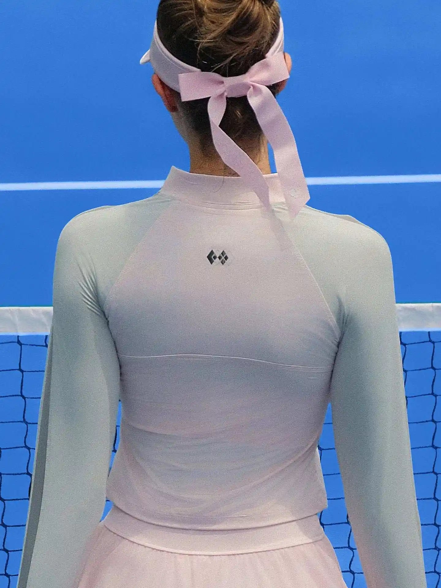 Pink long-sleeve fitted top with a half-zip neckline and subtle logo detail, styled on the tennis court.