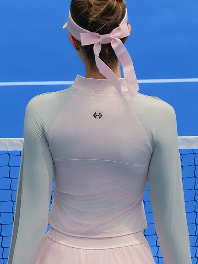 Pink long-sleeve fitted top with a half-zip neckline and subtle logo detail, styled on the tennis court.