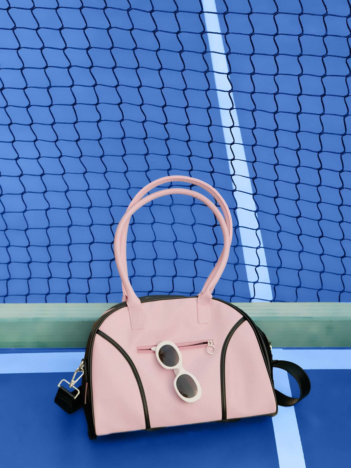 Soft pink dome-shaped tennis bag featuring Pom Pêche logo, styled with black trim and placed on a tennis court.