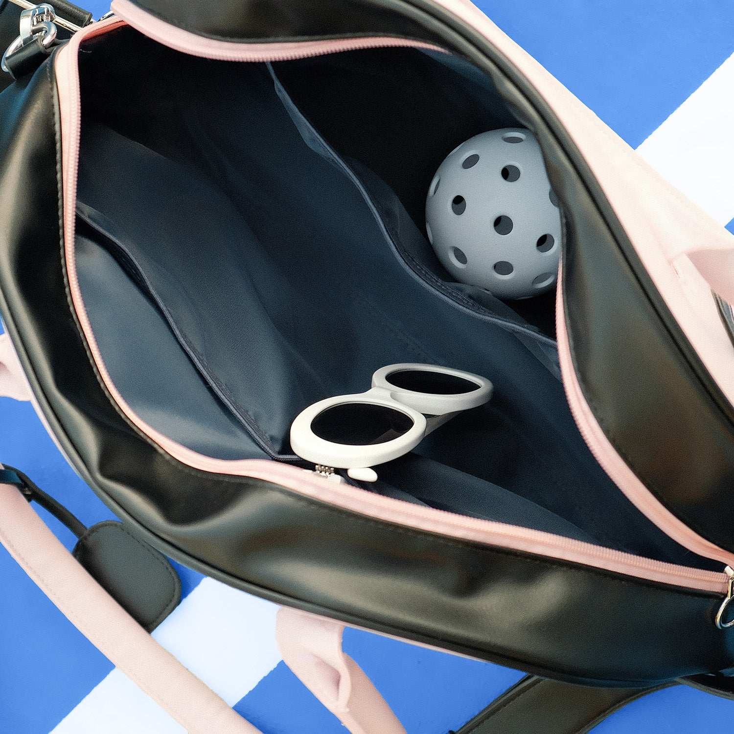Soft pink dome-shaped tennis bag featuring Pom Pêche logo, styled with black trim and placed on a tennis court.