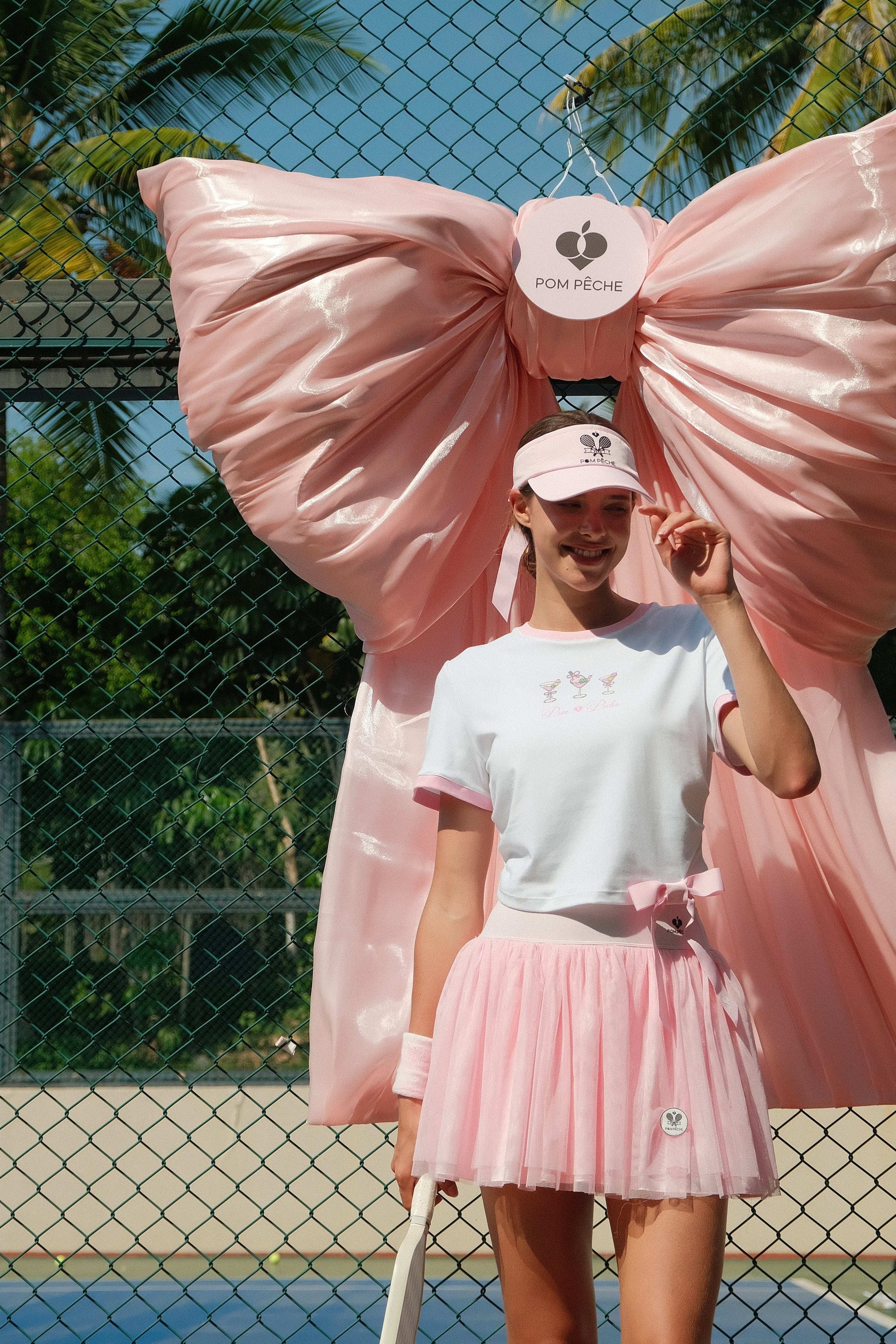 Model in pink puff tulle tennis skirt walking on blue court, showing soft layered movement and high-waisted tennis skirt style.