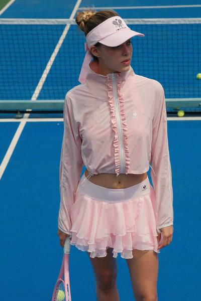 Soft pink cropped jacket with ruffled zip-front detail and long sleeves, styled on the tennis court.