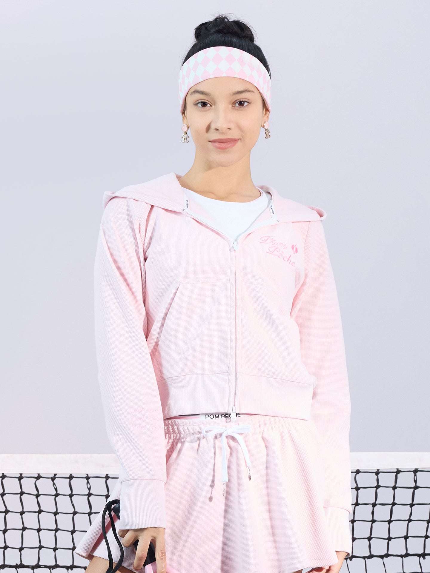 Soft pink zip-up hoodie with bow detail on the hood and embroidered logo, perfect for warm-ups or everyday wear.