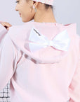Soft pink zip-up hoodie with bow detail on the hood and embroidered logo, perfect for warm-ups or everyday wear.