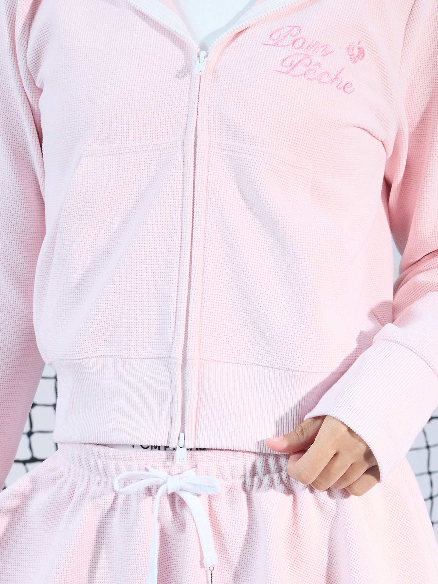 Soft pink zip-up hoodie with bow detail on the hood and embroidered logo, perfect for warm-ups or everyday wear.