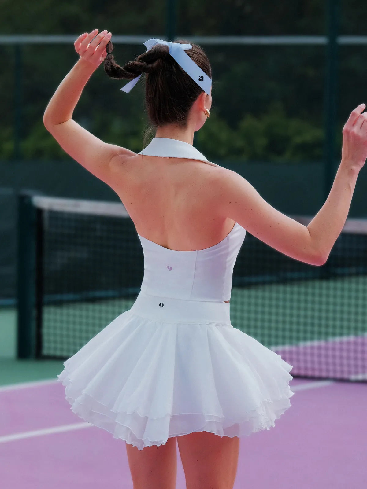 Woman in a white tennis dress on a tennis court with her arms raised.