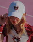 Person wearing a white cap and matching outfit with heart designs on a pink background