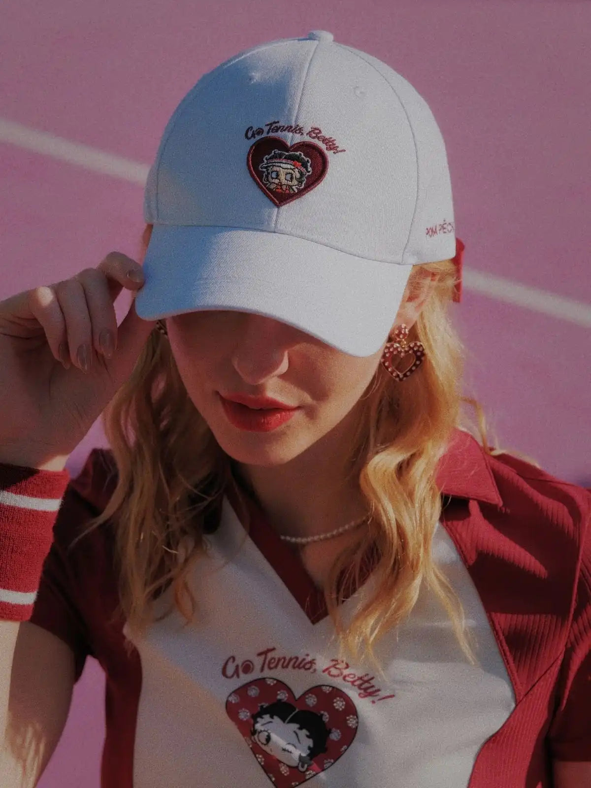Person wearing a white cap and matching outfit with heart designs on a pink background