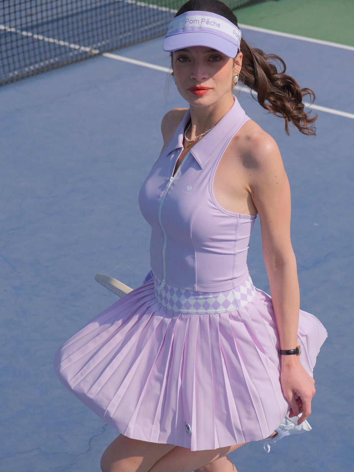 A purple pleated tennis skirt with an argyle waistband is shown flowing on court, styled as a lightweight athletic skirt for training.