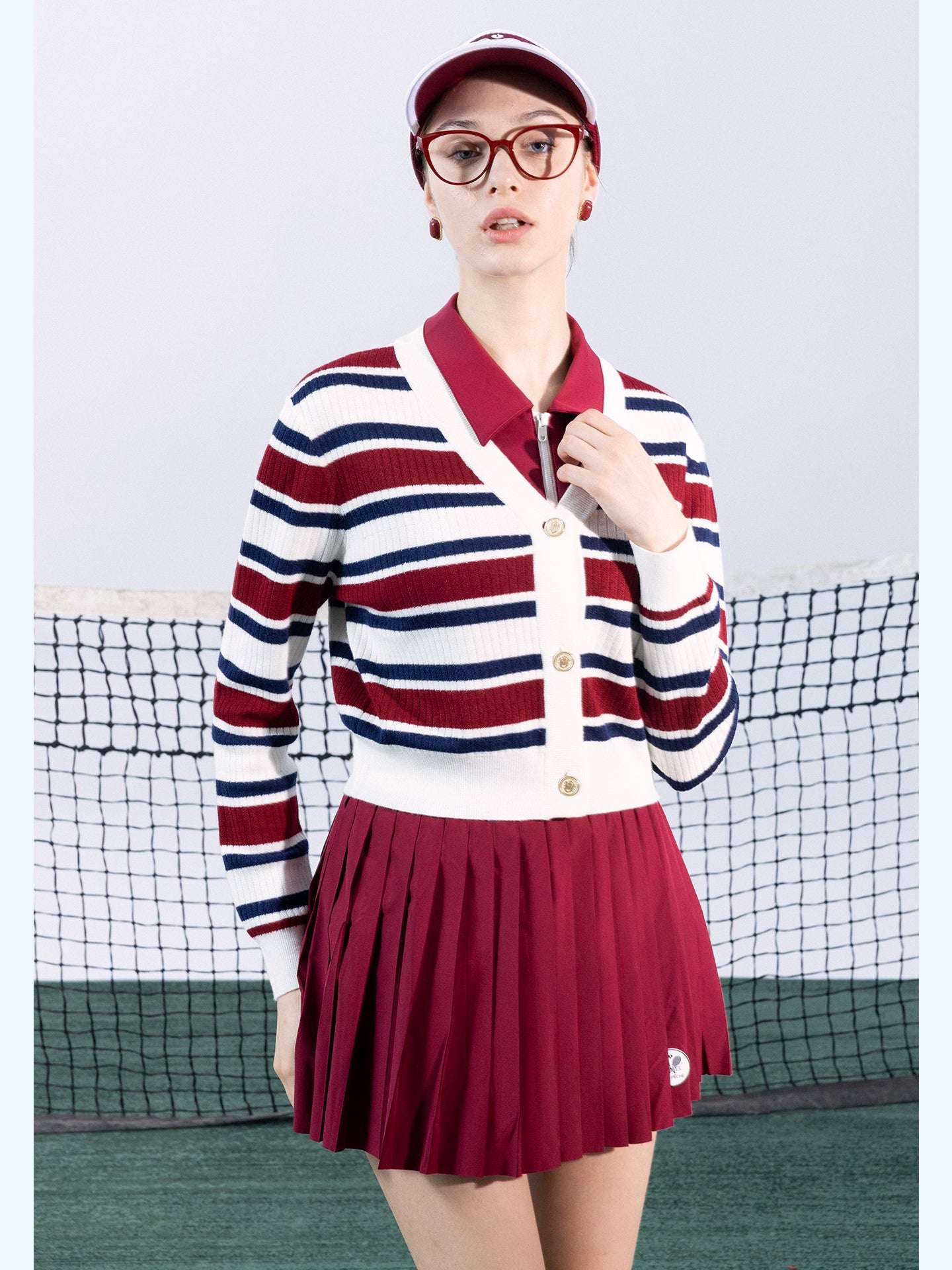 Red, navy, and white striped cardigan with a V-neck, button-down design, featuring an embroidered logo. Styled from court to café.