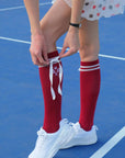 Person wearing red knee-high socks with white ribbons on a blue tennis court.