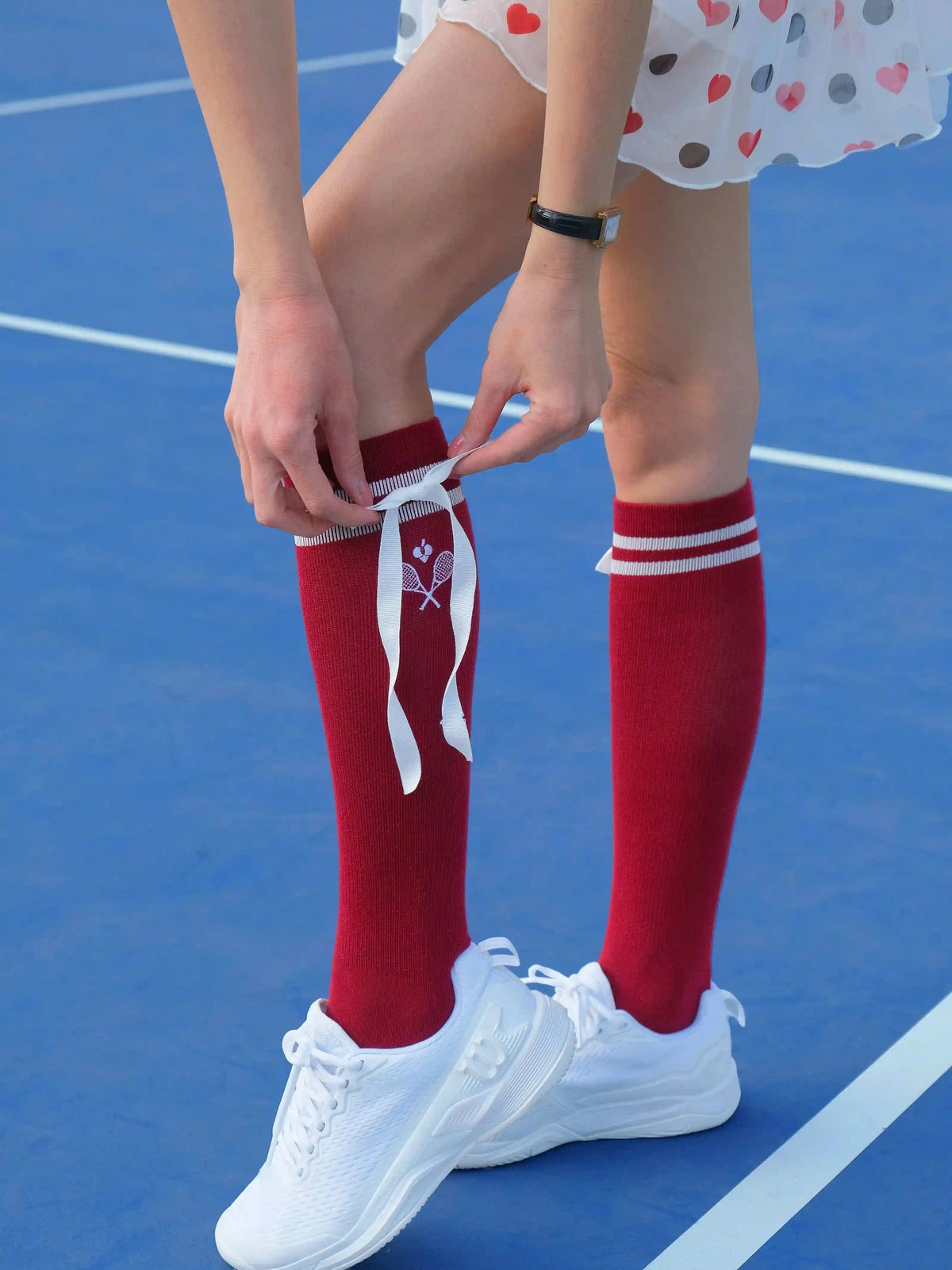 Person wearing red knee-high socks with white ribbons on a blue tennis court.