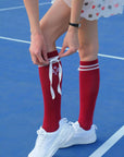Person wearing red knee-high socks with white ribbons on a blue court.