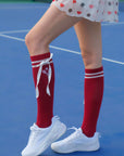 Person wearing red knee-high socks with white ribbons on a blue tennis court.