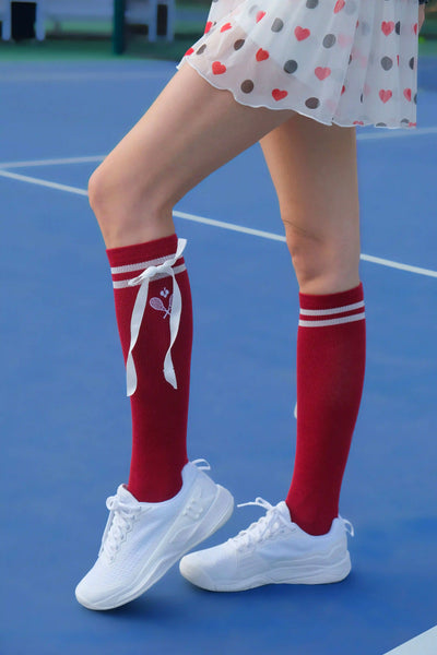 Person wearing red knee-high socks with white ribbons on a blue tennis court.