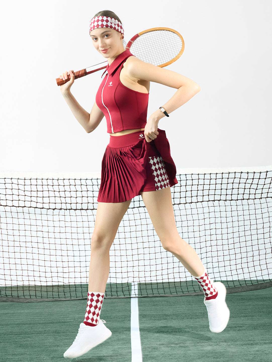 Red pleated tennis skirt with asymmetrical panels shown in motion, highlighting sporty movement and a high-waisted athletic tennis skirt fit.