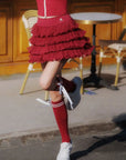 Person wearing a red dress with ruffles, red knee-high socks, and white sneakers on a street.